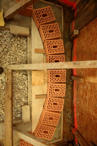 Um den Erdruck des Hanges besser abzufangen, mauern wir die Rückwand nun wie die Decke als Bogen. Die Holzschablone hilft, den Stich von 20 cm genau einzuhalten.