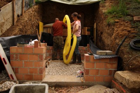 Zur Abdichtung wird die Mauer außenherum mit Bitumen eingeschmiert, dann kommt die Noppenbahn drumherum und dahinter das Drainagerohr. Was für ein Gefrickel. Diese gelbe Schlange ist sowas von widerspenstig!