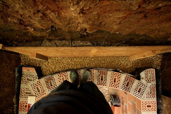 Die Schichten hinter dem Mauerwerk. Von "oben" nach "unten" bzw. von hinten nach vorne: Erdwand, die Füllung der abgerutschten Rückwand mit Stein- und Plattenresten, Rest vom Rettungsbauwerk aus USB-Platten (wird demnächst ganz entfernt), Kies, Noppenbahn. Nicht zu erkennen: Das Mauerwerk ist außen noch mit Bitumenfarbe bestrichen. Ja, und dann die Mauer.