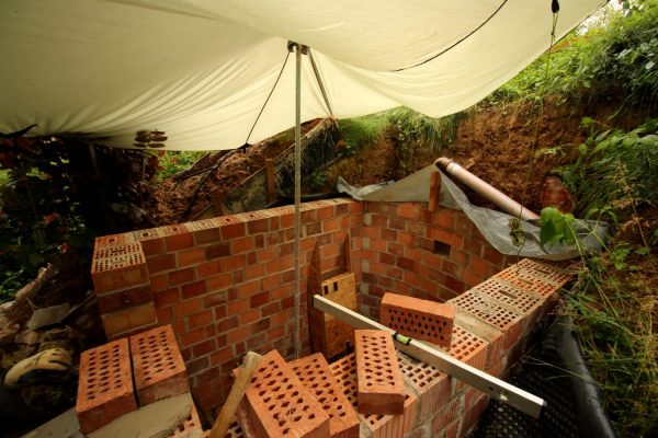 Blick in den noch offenen Erdkeller. Noch schützt das Tarp vor Regen und Sonne. Die letzte Mauerreihe wächst von links vorne gegen Uhrzeigersinn. Die Rundbogenschalung steht schon bereit.