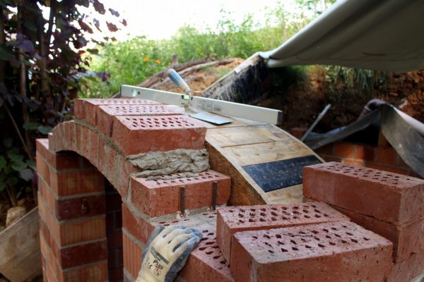 Also gleich die nächste Reihe oben drauf gemauert, damit das ganze nicht mehr so windig aussieht. Außerdem setzen wir zwei Eisenstangen auf jeder Seite, um die erste Reihe zusätzlich zu stützen.